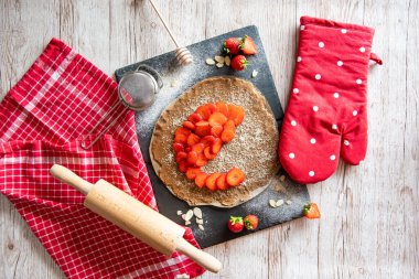 Çilekli ve bademli ev yapımı turtalı kek, siyah masa ve ahşap masa. Yanında yemek aletleri olan kırmızı havlu.