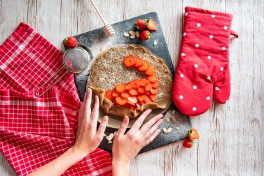 Çilek hazırlayan galette, fırın ellerinin ayrıntıları. Kek siyah masaya ve ahşap masaya yerleştirildi..