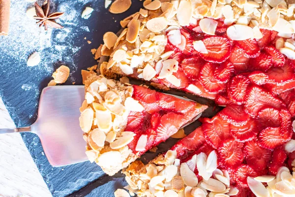 Çilekli ve bademli ev yapımı turtalı kek, siyah masa ve ahşap masa. Yanında yemek aletleri olan kırmızı havlu.