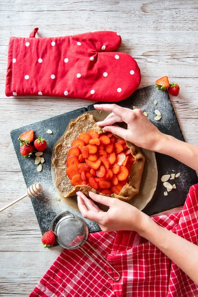 Çilek hazırlayan galette, fırın ellerinin ayrıntıları. Kek siyah masaya ve ahşap masaya yerleştirildi..