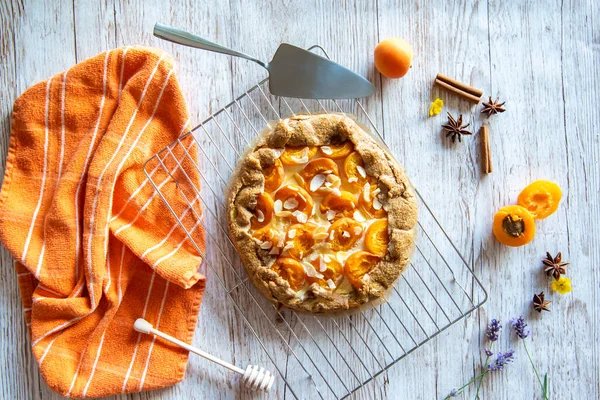 Apricot galette pie cake placed on wooden background with cooking tools on the side