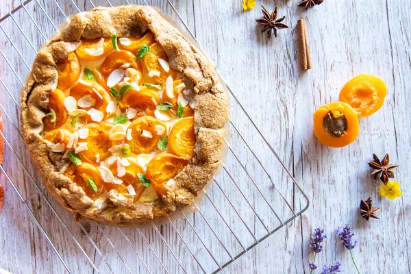 Apricot galette pie cake placed on wooden background with cooking tools on the side