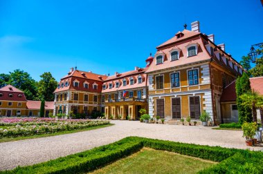 Güneşli bir yaz gününde, Rajec Jestrebi Şatosu 'nun panoramik manzarası. Mavi gökyüzü, çiçek açan pembe güller ve tarihi binanın önünde bir çeşme..