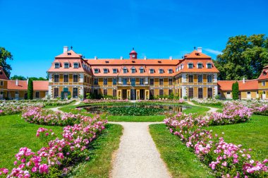 Güneşli bir yaz gününde, Rajec Jestrebi Şatosu 'nun panoramik manzarası. Mavi gökyüzü, çiçek açan pembe güller ve tarihi binanın önünde bir çeşme..