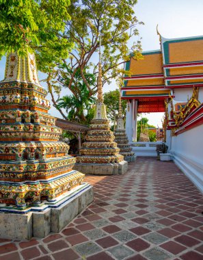 Wat Pho 'nun dış görünüşü, parlak güneşli bir günde Bangkok' ta açık mavi gökyüzünün altında parıldayan renkli çiçek seramikleriyle ve altın tapınak çatılarıyla süslenmiş..