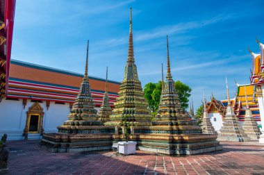 Wat Pho 'nun dış görünüşü, parlak güneşli bir günde Bangkok' ta açık mavi gökyüzünün altında parıldayan renkli çiçek seramikleriyle ve altın tapınak çatılarıyla süslenmiş..