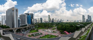 Bangkok, Tayland - 11.2025: Bangkok 'taki Lumphini Parkı yakınlarında metro hatları, hareket halindeki arabalar ve parlak kentsel gün ışığı altında modern gökdelenlerin ufuk çizgisi ile kalabalık bir kavşağın panoramik görüntüsü.