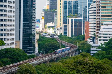 Bangkok, Tayland - 11.2025: Bangkok 'taki Lumphini Parkı yakınlarında metro hatları, hareket halindeki arabalar ve parlak kentsel gün ışığı altında modern gökdelenlerin ufuk çizgisi ile kalabalık bir kavşağın panoramik görüntüsü.
