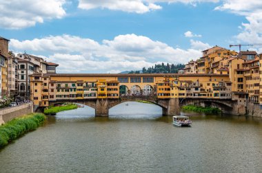Floransa 'daki Ponte Vecchio manzarası (Ponte Vecchio, Firenze) ve Arno Nehri yakınlarındaki binalar aydınlık bir yaz gününde, tarihi cazibe ve nehir kenarı manzarasını yakalar..