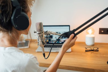 Genç kadın podcaster sesini mikrofona kaydediyor. Kadın radyo sunucusu stüdyosunda mikrofon ve dizüstü bilgisayar kullanarak podcast yapıyor.