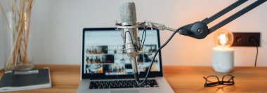 Podcast odasının içi. Canlı ses stüdyosu. Mikrofon, dizüstü bilgisayar, not defteri ve lamba masada. Geniş resim