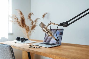 Yayın stüdyosu, iç mekan. Podcast için ev yapımı oda. Ses mikrofonu, tahta masadaki dizüstü bilgisayar.