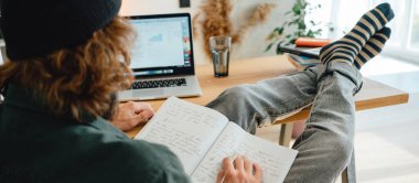 Sakallı öğrenci dizüstü bilgisayarla online sınavı geçmek için hazırlan. Üniversitedeki yetişkin adam ders çalışırken not alıyor.