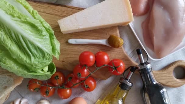 En el marco, un primer plano de los productos para la preparación de la ensalada César. Romaine, tomates, pechuga de pollo, salsa, aceite de oliva, queso parmesano, mostaza, ajo. — Vídeo de stock