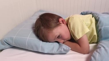 Çocuk sabah yatağında uyanır, gülümser ve saklanır. Mavi yatak, gözlerinin içine bak.