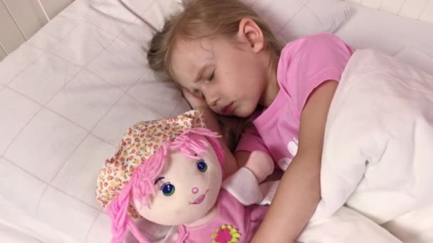 Klein meisje slaapt in bed, knuffelt haar favoriete speeltje. Zacht roze pop — Stockvideo