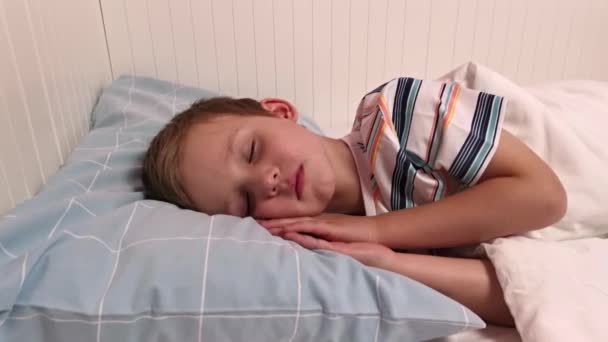 Маленький хлопчик спить у ліжку лежить на його боці. Хлопчик в смугастій піжамі — стокове відео