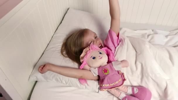 Niña duerme en la cama, abraza su juguete favorito. Muñeca rosa suave — Vídeos de Stock
