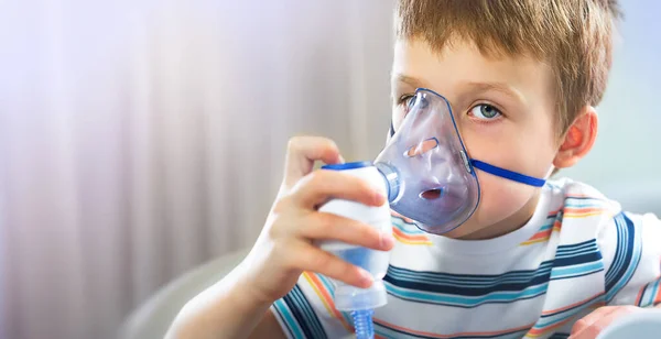 A boy in a blue T-shirt holds an inhalation mask near his face. The child treats colds, coughs at home. Free space for your design. Face close-up. The mask is in the foreground. — Stock Photo, Image