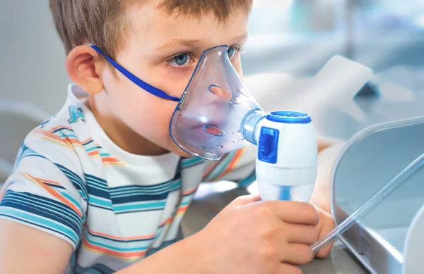 Mavi tişörtlü bir çocuk yüzünde solunum maskesi tutuyor. Çocuk soğuk algınlığını tedavi ediyor, evde öksürüyor. Tasarımın için boş yer. Yüzü yakın plan. Maske ön planda..