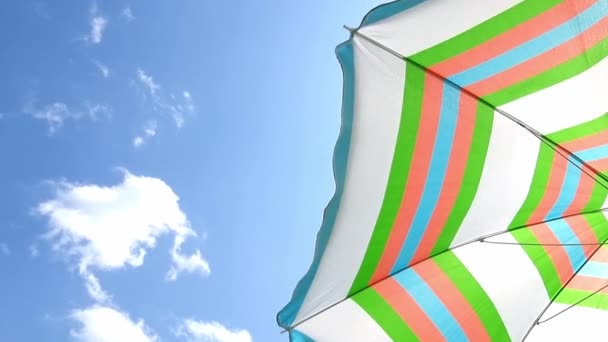 Μια προστατευτική ομπρέλα ενάντια στις ακτίνες του ήλιου σε φόντο γαλάζιου ουρανού και λευκών νεφών. Κίνηση ανέμου — Αρχείο Βίντεο