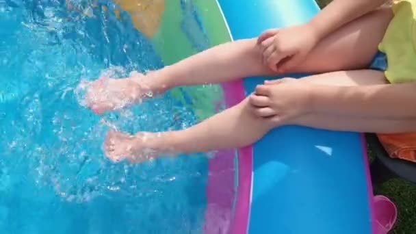 Маленькая девочка сидит на краю бассейна и размахивает ногами в воде — стоковое видео