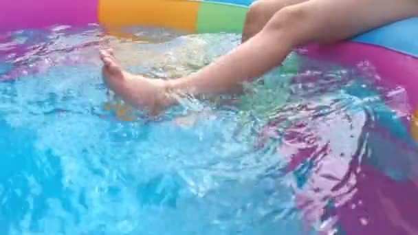 Klein meisje zit aan de rand van het zwembad en bungelt haar benen in het water — Stockvideo