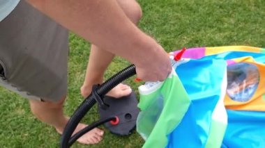 Bir adamın bacağı pompayla hava pompalar, açık havuzu şişirir. Yeşil çimen
