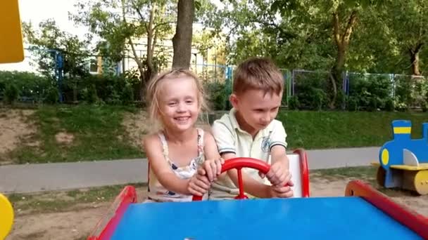 Ragazzo e ragazza oscillano su una macchina da scrivere per bambini all'asilo sullo sfondo di alberi verdi — Video Stock