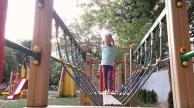 Bir kız çıplak ayakla dışarıda oyun parkında asılı bir kütükte yürüyor.