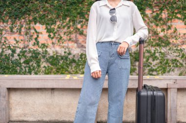 Ayakta duran ve siyah bavul taşıyan bir kadın yolcu. Havaalanında yolcu alımına gidiyor. Seyahat kavramı..