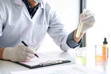 Laboratuvar önlüğündeki bilim adamı ya da tıp laboratuvar önlüğündeki deney tüpünü reaktörle tutarak cam şişede reaksiyonları karıştırarak kimyasal sıvı, laboratuvar araştırmaları ve testler içeren cam kaplar oluşturuyorlar..