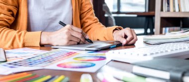 İş yerinde iş araçları ve aksesuarlarıyla renk seçimi ve grafik tableti üzerinde çalışan kadın yaratıcı grafik tasarımcı resmi.