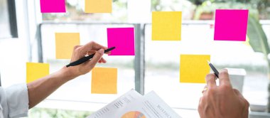 Finansal belge grafiğinde pazarlama büyümesi üzerinde çalışan iş ekibi istatistikleri raporlayarak, cam duvara yapıştırdığı notları kullanarak, strateji planı yazma konusunda başarı elde etmeye çalışıyor..