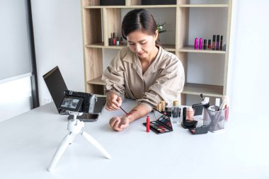 Mutlu gülümseyen zarif kadın blogcu, makyaj malzemesi kozmetik inceleme ürünü sunuyor ve kamera ekranında sosyal ağa canlı yayın yapan video bloglarını öğretiyor..