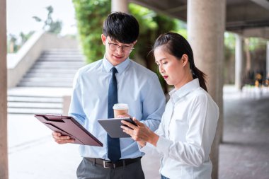 Elinde tablet olan genç iş kadını elinde kahve fincanı tutarken ve iş projesinden bahsederken genç iş adamına yapılan bu sunum yatırımına bakıyor.