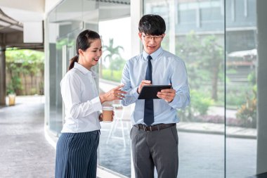 Genç iş ortağı, elinde kahve fincanı tutarken ve bu tableti yatırım planlamaya bakarken iş projesi hakkında konuşmak için tablet kullanıyor.