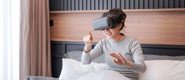 Sanal gerçeklik gözlüğü takan Asyalı genç bir kadının oyun oynarken, dinlenirken ve yatak odasında yatakta otururken fotoğrafını çek.