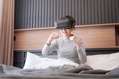 Sanal gerçeklik gözlüğü takan genç Asyalı kadın boks maçına giderken dinleniyor ve yatak odasında yatakta oturuyor.