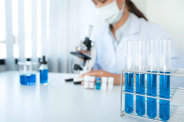 Orvosi Maszkos Tudós Mikroszkóppal Kémcsővel Kék Folyadékkal Miközben Coronavirus Vakcinával — Stock Fotó