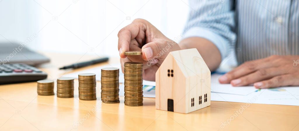 Asian business man putting coin increase on coins stacking with house model while preparation to saving for property investment and house mortgage