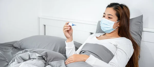 의료용 마스크를 아시아 아프다고 느끼며 침대에 담요를 체온을 측정하기 체온계를 — 스톡 사진