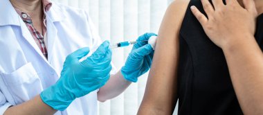 Doktorun hastane randevusu sırasında kovid 19 salgınından korunmak için hastanın omzuna koronavirüs aşısı enjekte eden tıp eldivenli doktor.