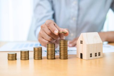 Asyalı işadamı, emlak yatırımı ve konut kredisi için tasarruf yapmaya hazırlanırken ev modelinin yanında madeni paralara zam yapıyor.