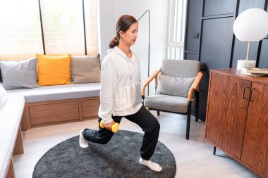 Asyalı bir kadın, evde egzersiz yaparken, güçlü bacaklar ve kollar için vücudunun yan tarafında halterle yoga egzersizi yapıyor.