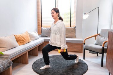 Asyalı bir kadın, evde egzersiz yaparken, güçlü bacaklar ve kollar için vücudunun yan tarafında halterle yoga egzersizi yapıyor.