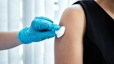 Doktorlar ellerinde şırınga ve pamuk tutarak hastanın omzuna koronavirüs aşısı enjekte ediyorlar. Doktorun hastaneden randevu aldığı sırada kovid-19 salgınından korunmak için.