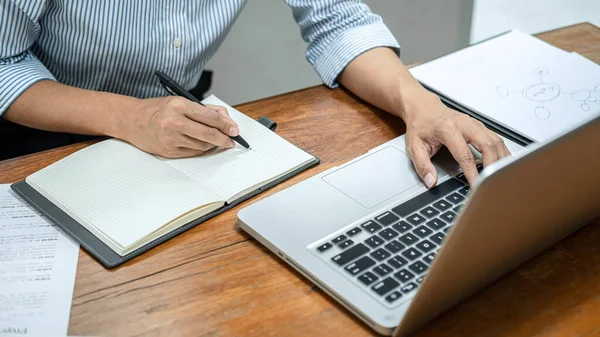 Business woman reading business report to checking financial data on laptop and writing information on document while sitting to working from home