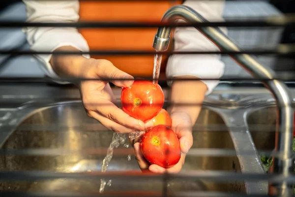 Hands of asian housewife washing tomato and vegetables with water in sink while wearing apron and preparing to cooking for healthy meal in the kitchen at home
