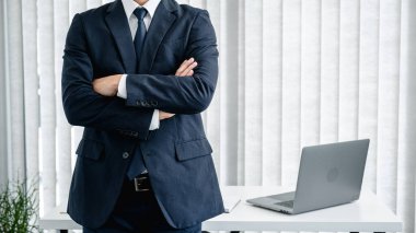 Takım elbiseli bir işadamının görüntüsü kollarını kavuşturmuş ve ofisteki kameraya bakarken yeni iş projesiyle ilgili çalışmada kendine güveni tamdır.